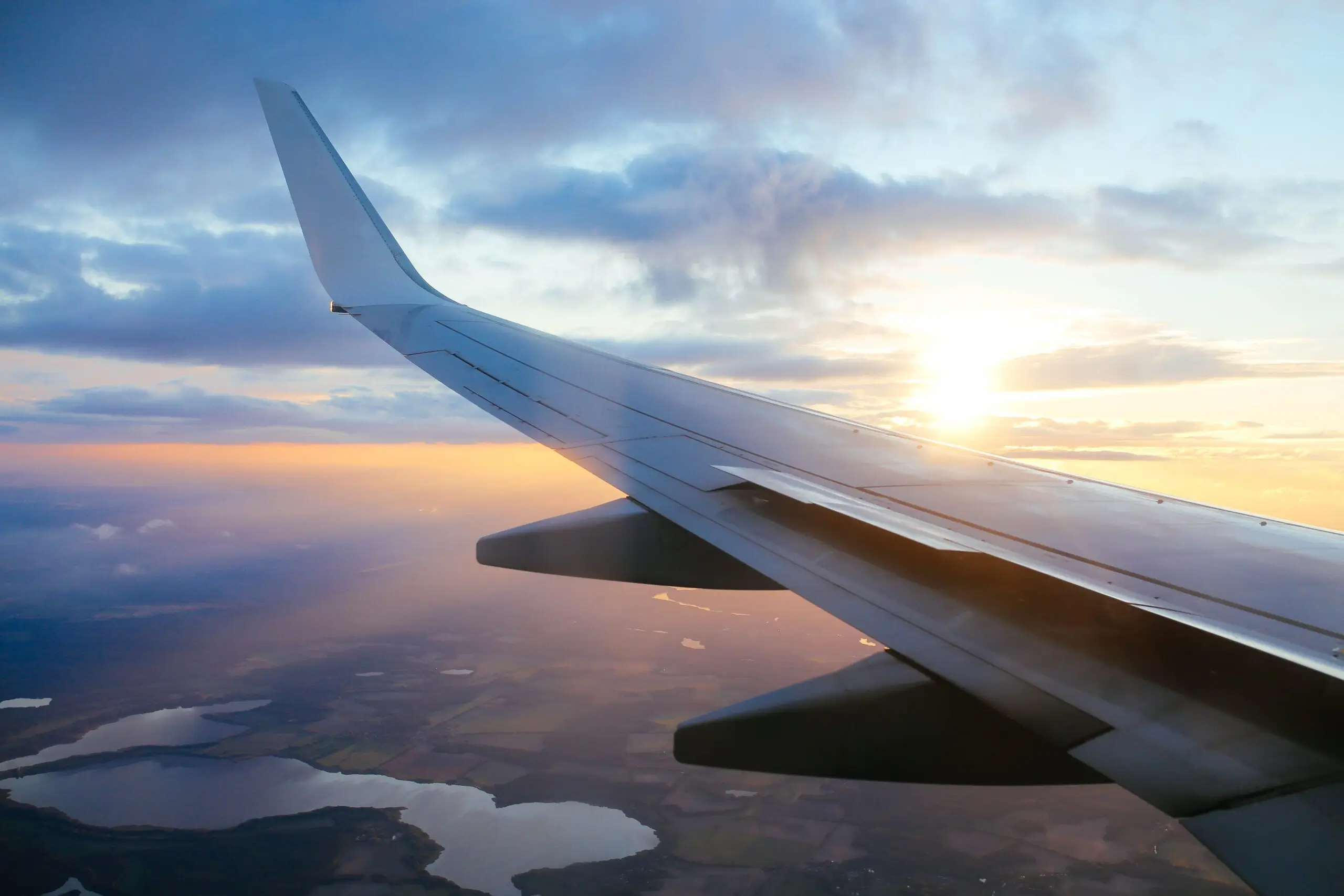 A view from an airplane window showing the wing with a beautiful sunset in the background, representing travel, aviation, and the serenity of flying above the clouds.